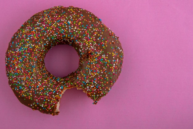 Top view of chocolate bitten donut on a pink surface