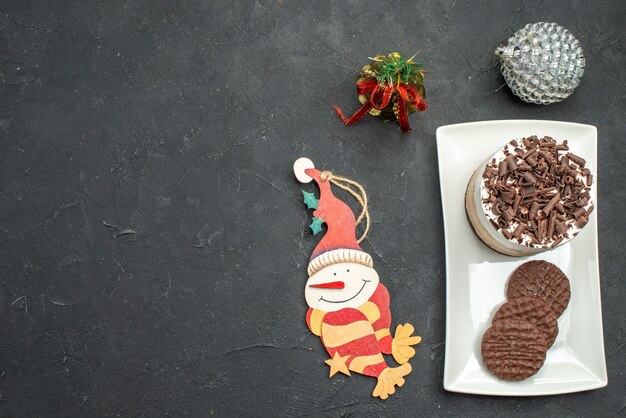 無料写真 暗い孤立した背景の上の白い長方形のプレートのクリスマスツリーのおもちゃの上面図チョコレートケーキとビスケット