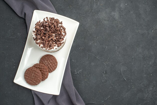 Top view chocolate cake and biscuits on white rectangular plate and purple shawl on dark isolated background