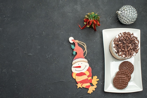Top view chocolate cake and biscuits on white rectangular plate xmas tree toys on dark isolated background