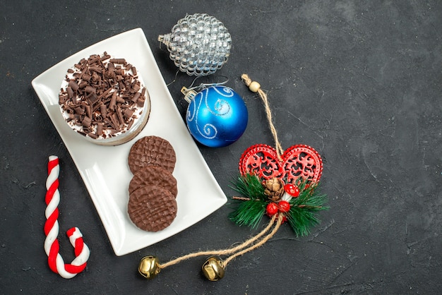 Top view chocolate cake and biscuits on white rectangular plate xmas tree toys on dark isolated background