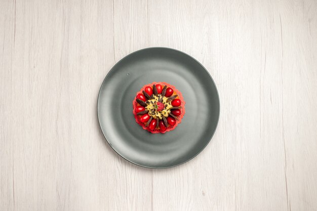 Top view chocolate cake rounded with cornel and raspberry in the center in the grey plate on the white wooden background