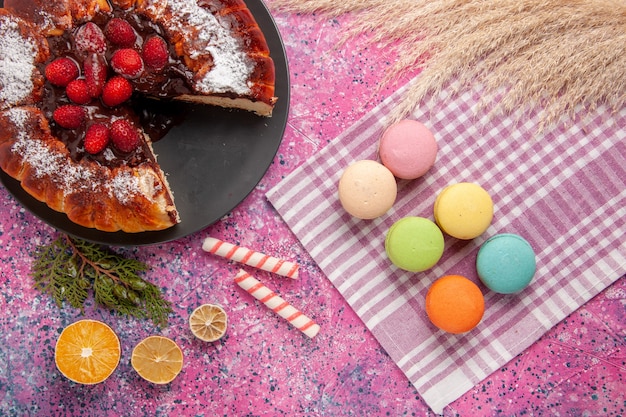 Бесплатное фото Вид сверху шоколадный торт с клубникой и макаронами на розовом столе, сахарное сладкое печенье