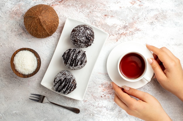 Вид сверху шоколадные торты с чашкой чая и кокосом на белой поверхности шоколадный торт бисквитное сахарное сладкое печенье