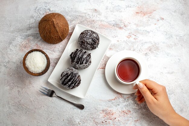 Вид сверху шоколадные торты с чашкой чая и кокосом на белой поверхности шоколадный торт бисквитное сахарное сладкое печенье