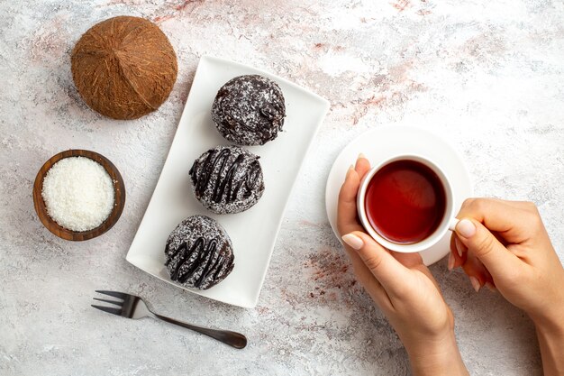 Top view chocolate cakes with cup of tea and coconut on white surface chocolate cake biscuit sugar sweet cookies