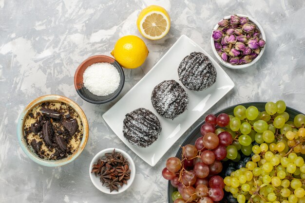 Top view chocolate cakes with lemon and grapes on white surface