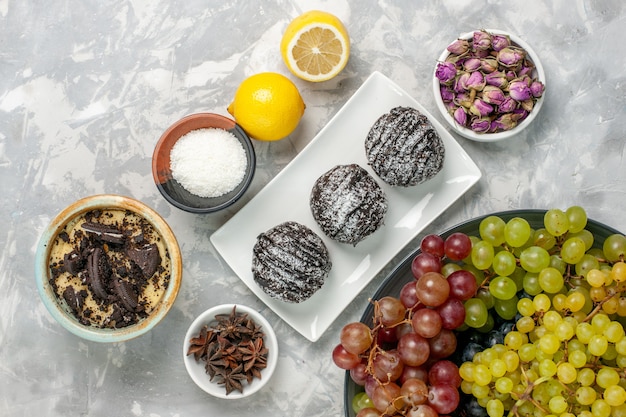 Top view chocolate cakes with lemon and grapes on white surface