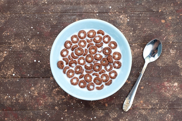 Top view chocolate cereals with milk inside blue plate and along with spoon on brown