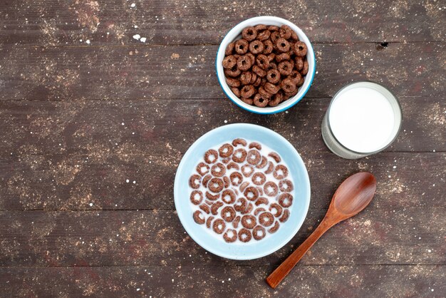 Top view chocolate cereals with milk inside blue plate and along with spoon on brown