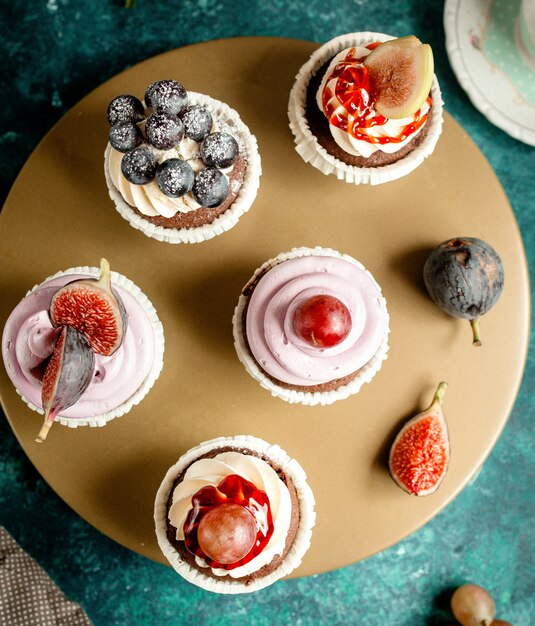 Free photo top view of chocolate cupcakes decorated with vanilla cream figs grapes and blueberries