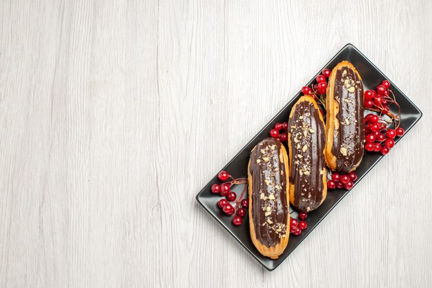 흰색 나무 바닥의 오른쪽에있는 검은 색 등각 투영 직사각형 접시에 상위 뷰 초콜릿 eclairs 및 건포도