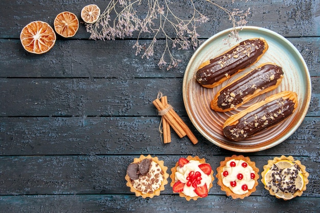 Top view chocolate eclairs on oval plate tarts cinnamon dried oranges on the dark wooden table with copy space