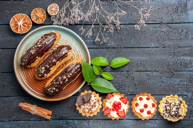 Top view chocolate eclairs on oval plate tarts laeves cinnamon dried oranges and on the dark wooden table with copy space