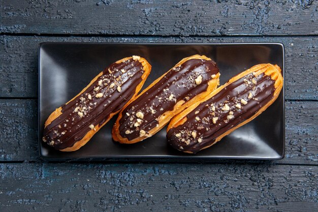 Top view chocolate eclairs on rectangle plate on dark wooden surface