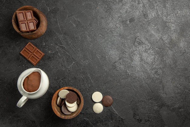 Free photo top view chocolate on the table chocolate and chocolate cream in the wooden bowls on the black table