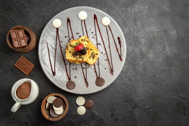 Top view chocolate on the table plate of cake with chocolate-covered strawberries and chocolate and chocolate cream in the wooden bowls on the black table