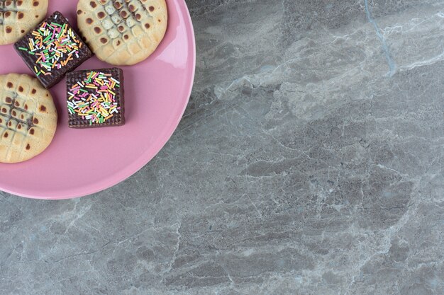 Top view of chocolate wafer and cookies on pink plate.