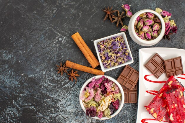 Top view of chocolates on white plate with bowls of dried flowers and cinnamon on grey ground