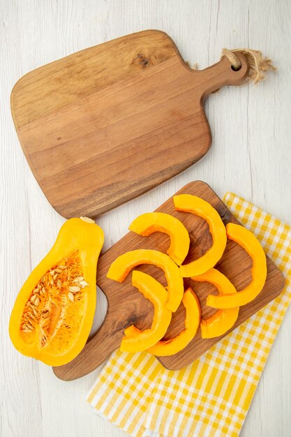 Top view chopped butternut squash on chopping board on yellow white checkered kitchen towel cutting board on grey table