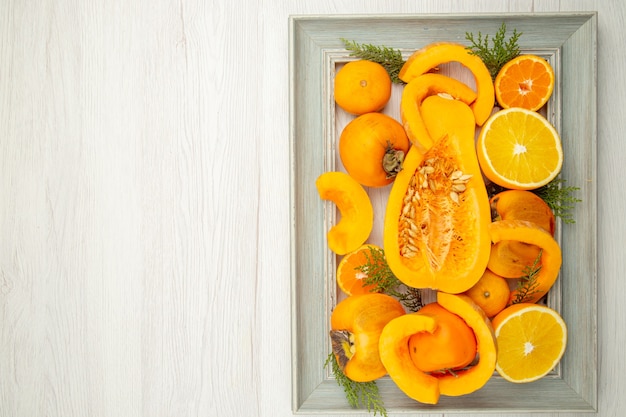 Вид сверху нарезанный мускатный орех, тыква, хурма, мандарины, половина апельсина на рамке