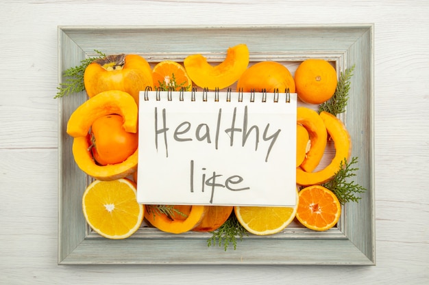 Бесплатное фото Вид сверху нарезанный мускатный орех, тыква, хурма, мандарины, половина апельсина на рамке здорового образа жизни, написано в блокноте