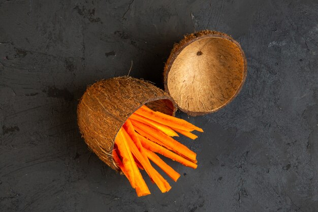 Top view chopped carrots in a coconut shell on black