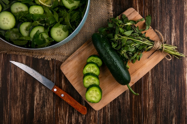 Foto gratuita vista dall'alto di cetrioli tritati con menta in una padella con un tagliere e un coltello su una superficie di legno