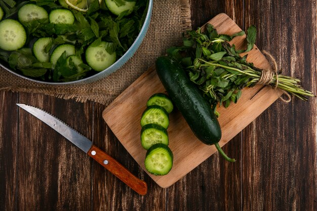 Top view of chopped cucumbers with mint in a pan with a cutting board and knife on a wooden surface