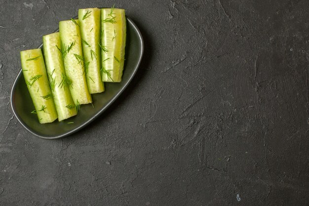 Top view of chopped fresh cucumber served with green on a black plate on dark wall