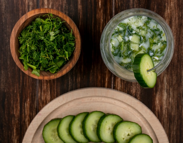 Top view of chopped greens with okroshka and cucumbers on a stand on a wooden surface