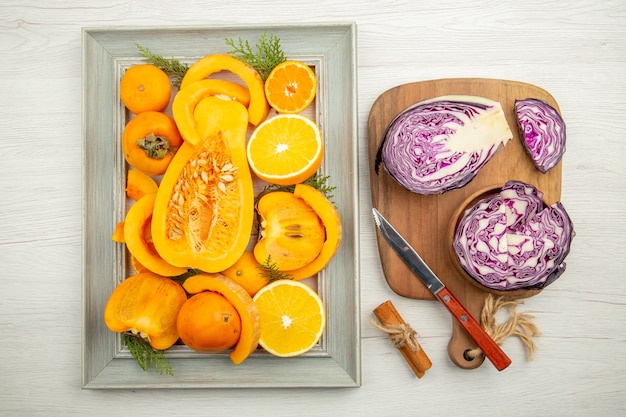 Top view chopped red cabbage in bowl knife on cutting board cinnamon cut squash persimmon cut oranges on frame on grey background