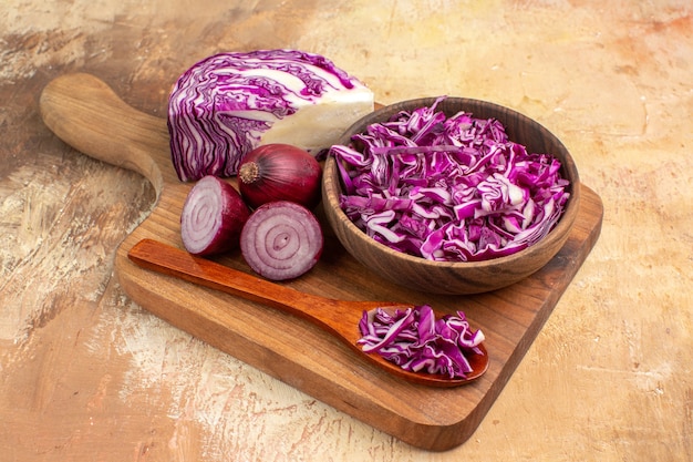 Top view chopped red cabbage in a bowl and some onions on a wooden cutting board for preparation of homemade salad on a wooden background with copy space