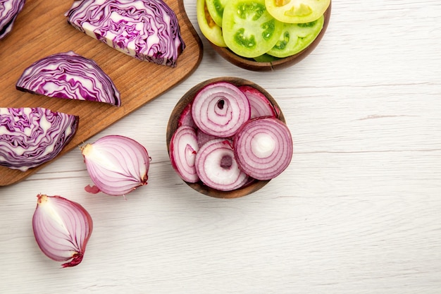 Top view chopped red cabbage on wood board cut green tomatoes cut onion in bowls on white table free space