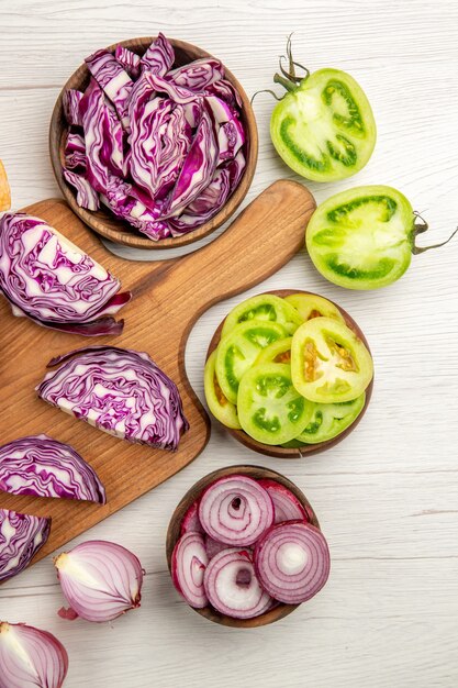 Top view chopped red cabbage on wood board cut onion cut green tomatoes in bowl on white table