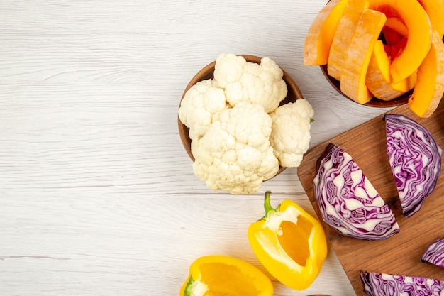 Top view chopped red cabbage on wood board cut yellow bell peppers cauliflower cut pumpkin in bowls on white table free place