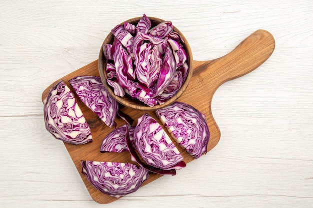 Top view chopped red cabbages in wooden bowl on cutting board on white surface