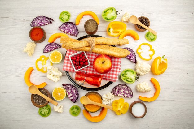 Вид сверху нарезанные овощи яблочный хлеб красная бутылка на салфетке на белом блюде различные специи в небольших мисках на столе