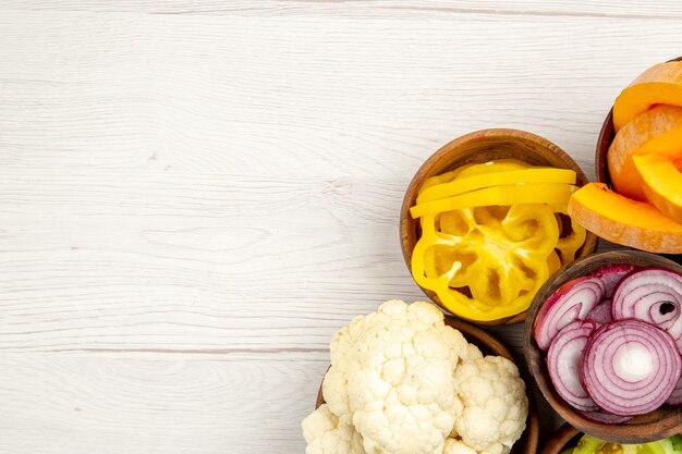 Top view chopped vegetables cut pumpkin cut yellow bell peppers cut onion cauliflower in bowls on white table free space