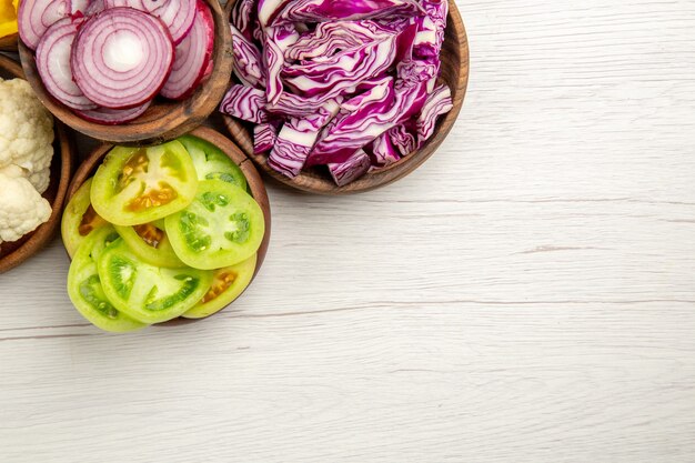 Top view chopped vegetables cut red cabbage cut onion cut green tomatoes cauliflower in bowls on white table free space