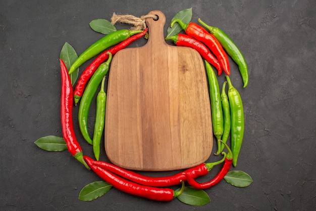 Free photo top view a chopping board in the circle of red and green hot peppers and pay leaves on black background