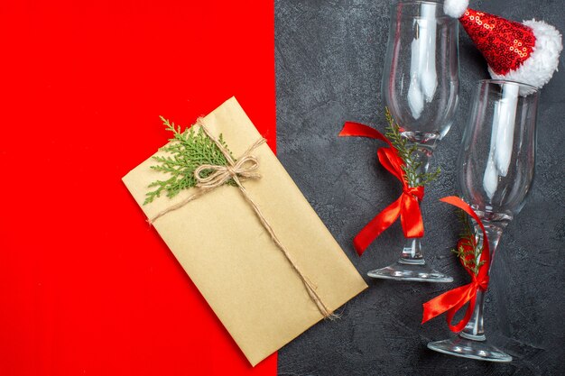 Top view of Christmas background with santa claus hat glass goblets and gift on red and black background