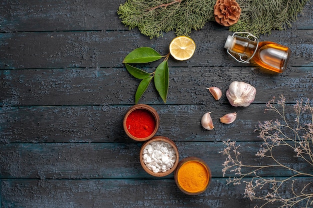 Free photo top view christmas dish bottle of oil bowls of spices lemon garlic spruce branches with cones on the dark table