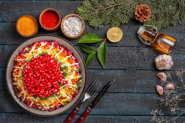 Top view Christmas dish dish bottle of oil garlic next to the fork and knife bowls of different spices lemon spruce branches with cones on the table