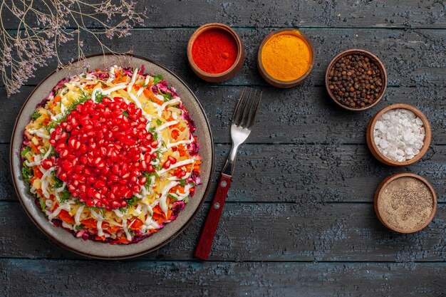 Top view Christmas food five bowls of colorful spices next to the fork Christmas dish with seeds of pomegranate and tree branches