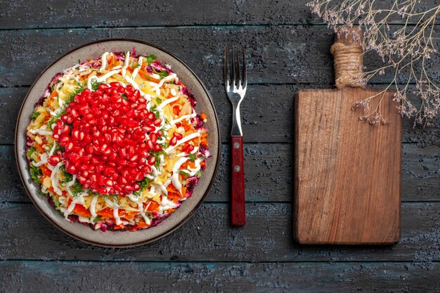 Top view Christmas food tasty Christmas dish with seeds of pomegranate next to the fork and cutting board on the grey table