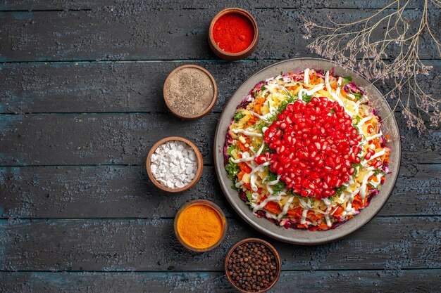 Top view Christmas food white plate of Christmas dish with seeds of pomegranate next to the tree branches and bowls of colorful spices on the table