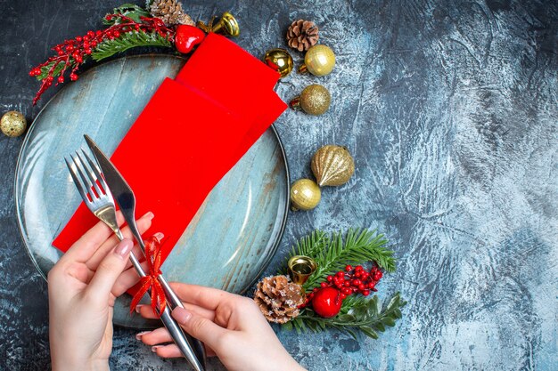 Top view of Christmas mood with hand setting a table layout with cutlery set and blue plate on dark background