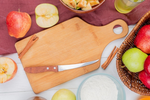 Top view of cinnamon and knife on cutting board with apples flour apple juice on bordo cloth and wooden background