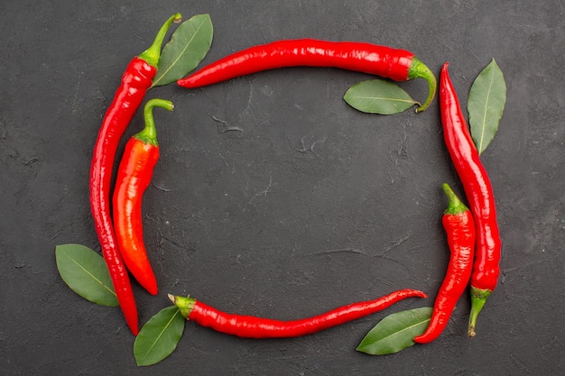 Top view the circle of red hot peppers and pay leaves on a black table